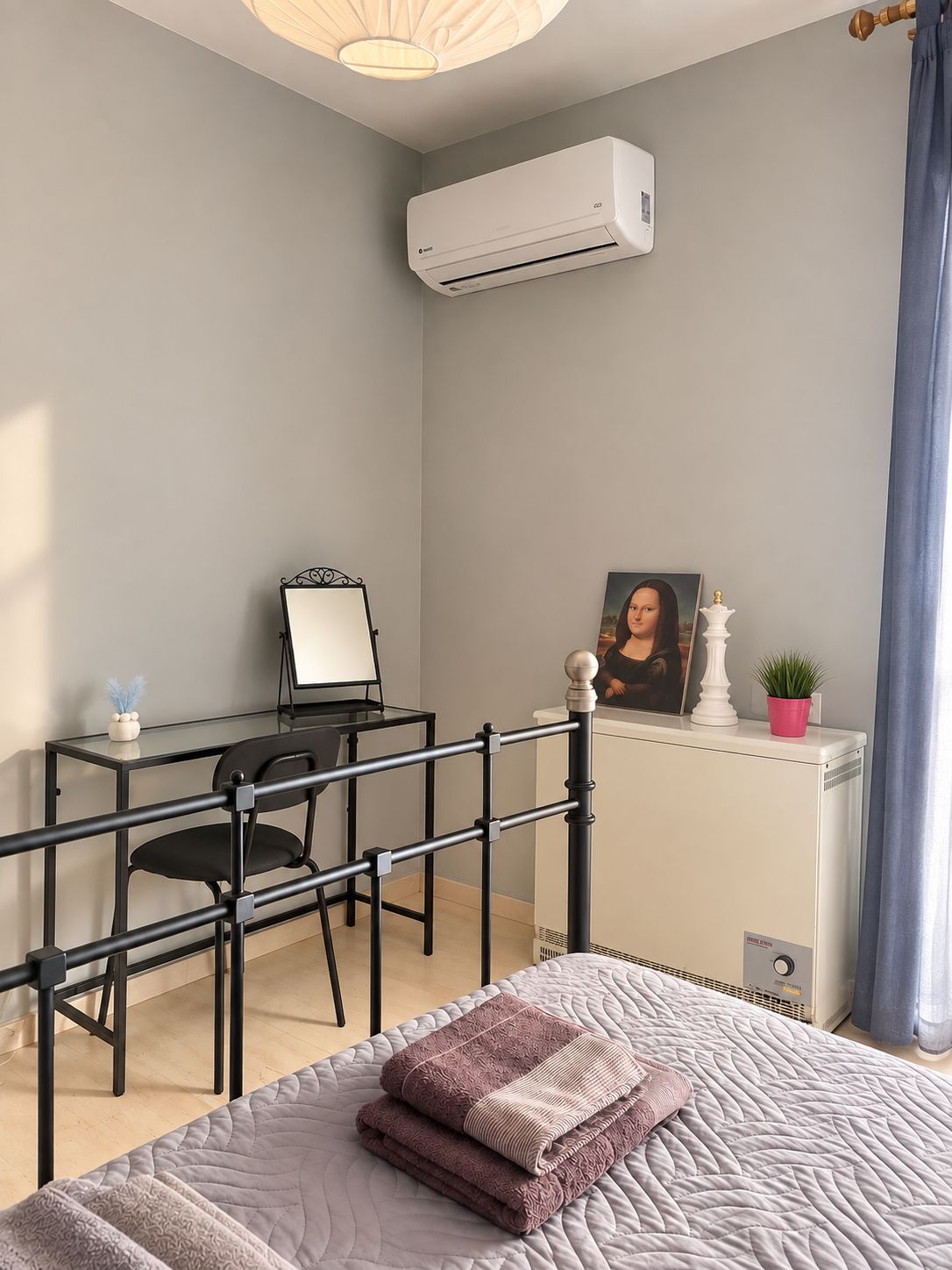 Un dormitorio con cama, escritorio, silla, aire acondicionado, marco de fotos y radiador.