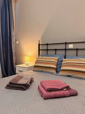 A neatly made bed with striped pillows, a bedside lamp, and folded towels on a textured bedspread. - Windsor Place - Self Check in With Code (Vari-Voula-Vouliagmeni)