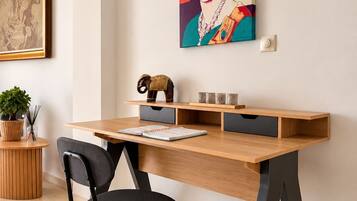 A modern office space with a wooden desk, black office chair, and a painting of a woman on the wall.