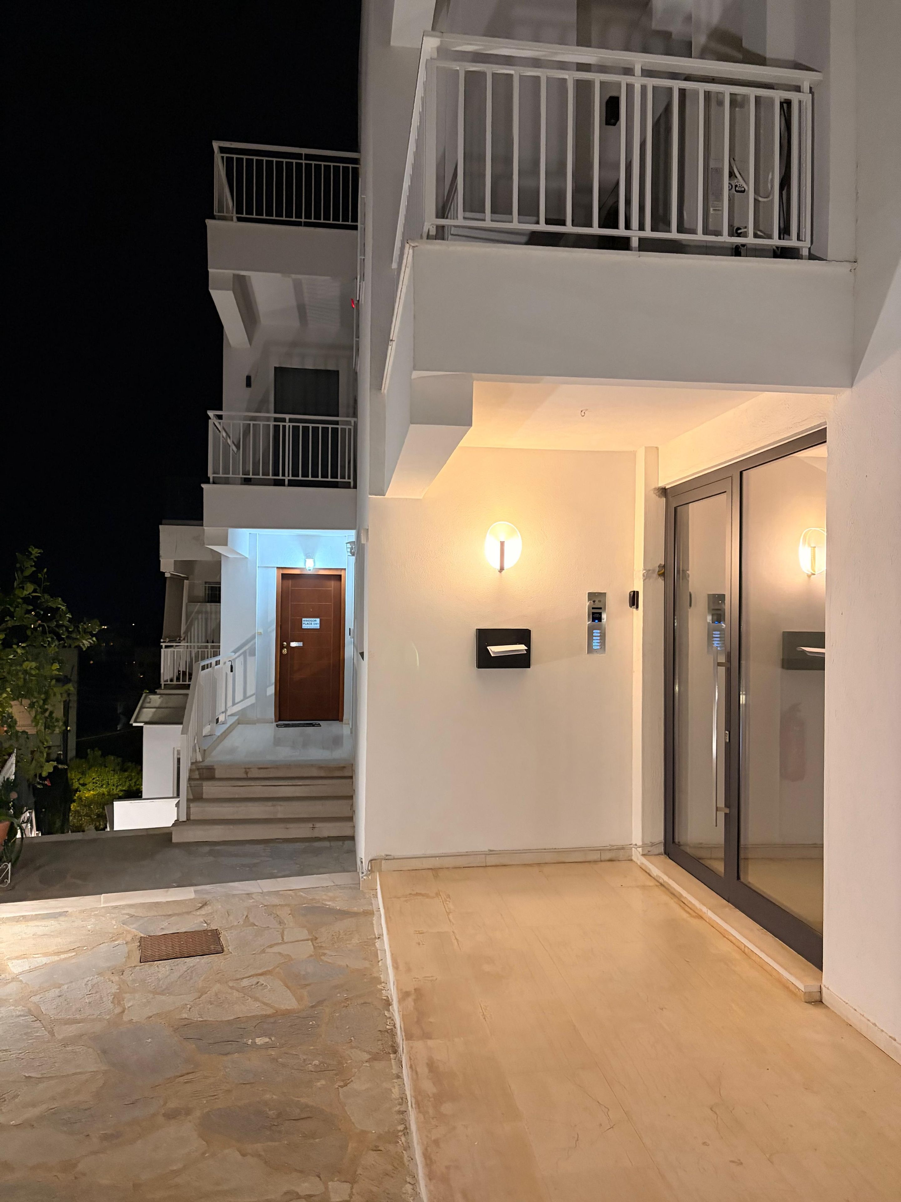 Um edifício com vários andares, com uma escadaria que leva à entrada, uma caixa de correio e uma porta de vidro.
