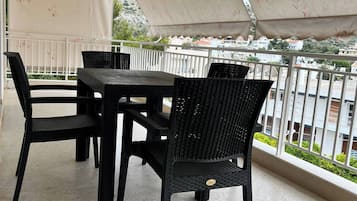 Ein Balkon mit Gartenmöbeln, einem weißen Sonnensegel und Blick auf Gebäude im Hintergrund.
