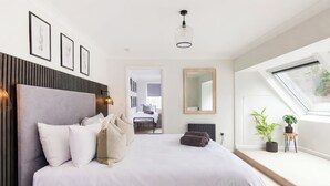 Un dormitorio moderno con una cama grande, mesitas de noche, tragaluces, un espejo y obras de arte enmarcadas en la pared.