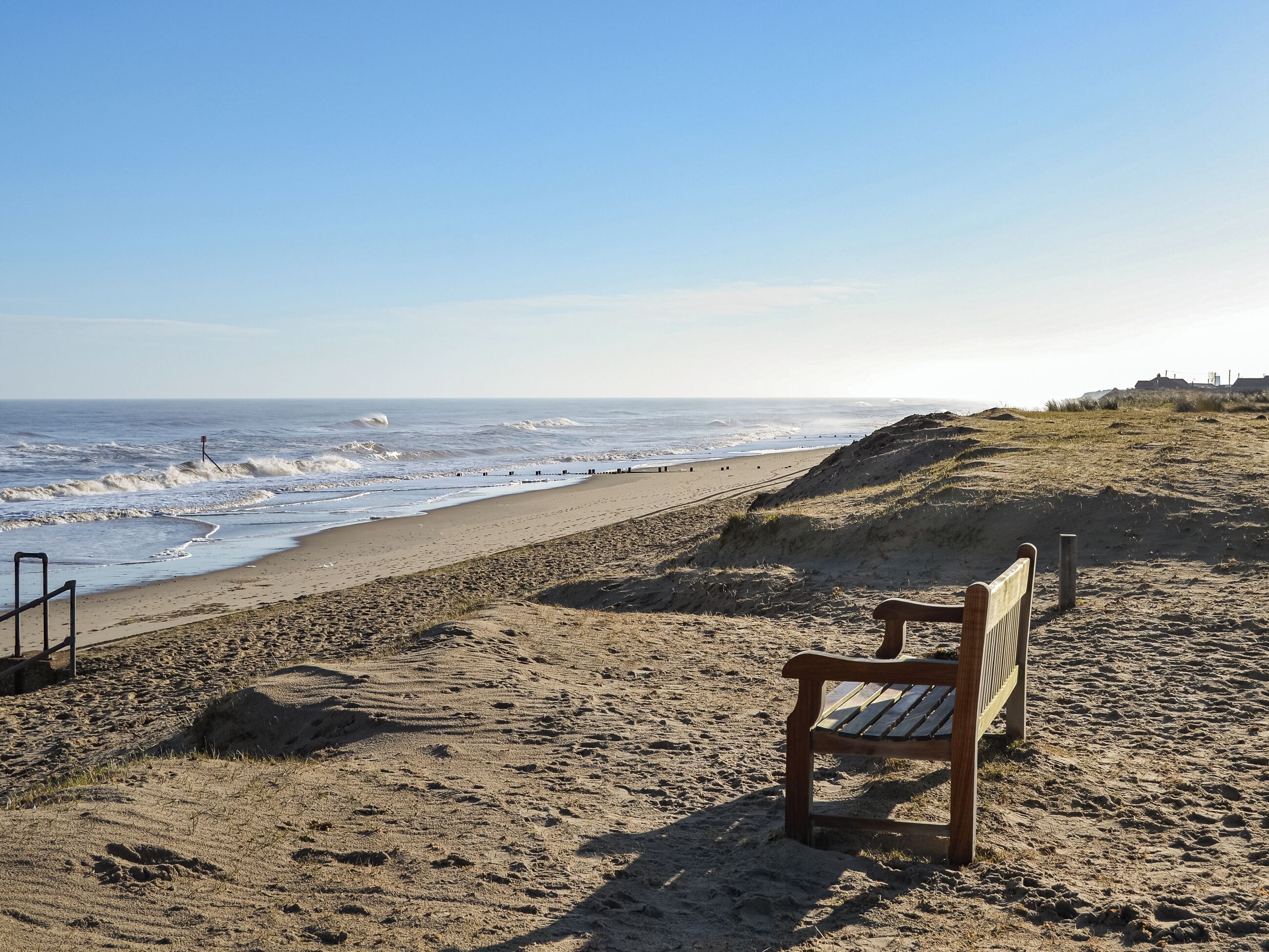 A sandy beach with a wooden bench and a railing, overlooking the ocean.