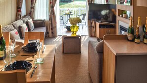 A cozy RV interior with a dining area, sofa, TV, and a small balcony with a view of a house.