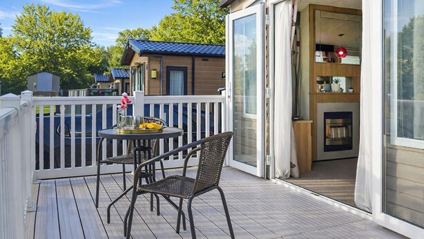 A wooden deck with a table and chairs, a sliding glass door leading to a kitchen area, and a white fence surrounding the deck.