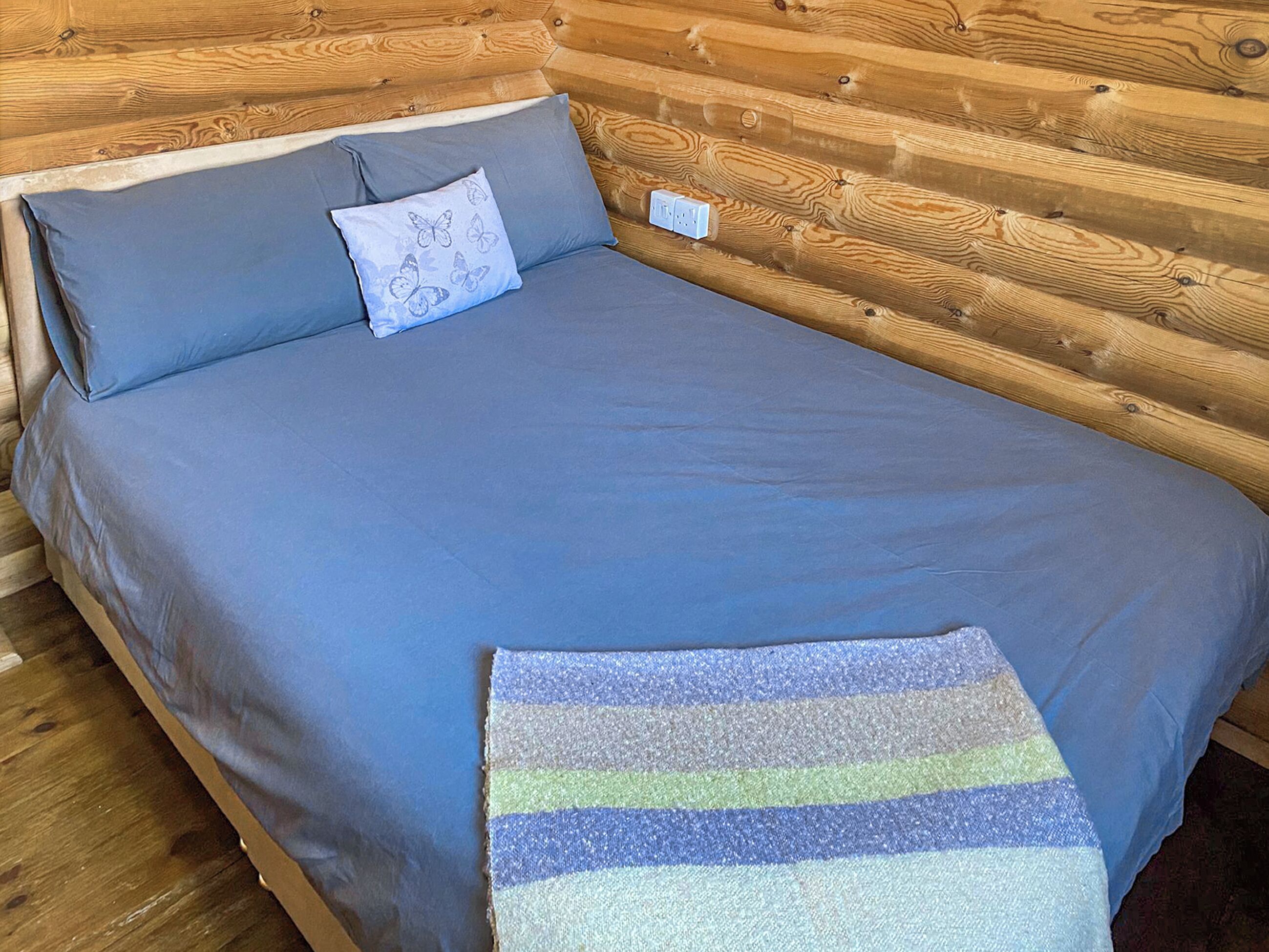 A bed with a blue mattress and pillows, a striped blanket, and a wooden cabin interior.