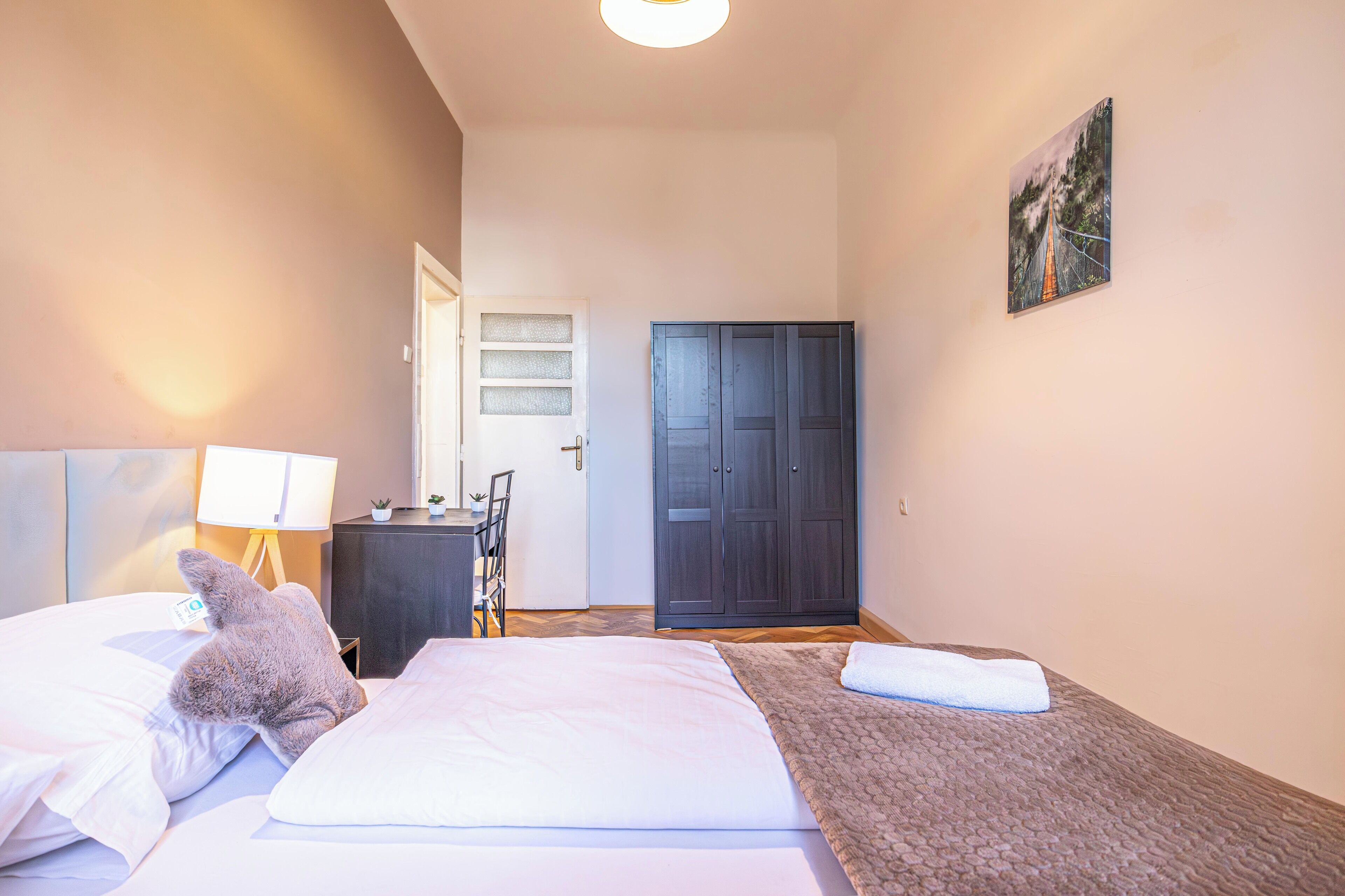 Een hotelkamer met een bed, een bureau, een stoel, een kledingkast en een schilderij aan de muur.