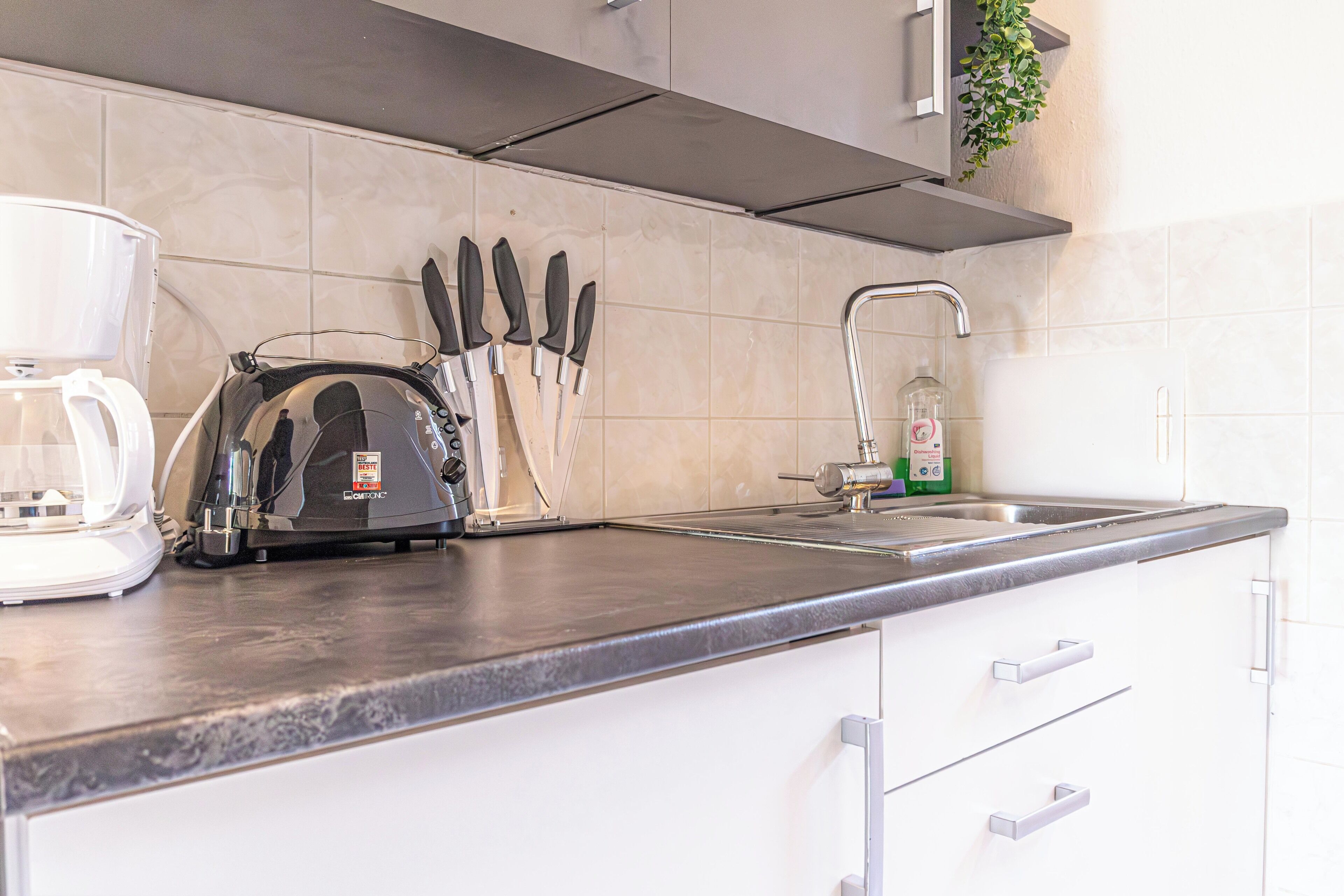 A kitchen with a coffee maker, knives, and a sink.