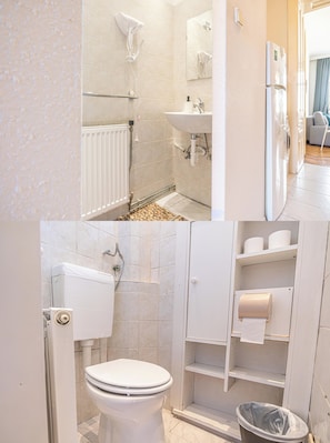 Et badeværelse med toilet, bruser, håndvask og toiletpapirholder.