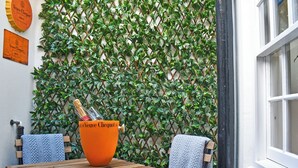 A wooden table with a large orange vase, two chairs, and a green leafy wall. - 2 bedroom accommodation in Whitby (Whitby)