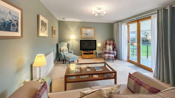 A living room with a sofa, armchairs, a coffee table, a television, and a balcony with a view. - Northbeach Apartment B (Prestwick)