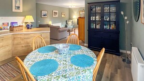 A cozy living room with a sofa, a dining table with chairs, a cabinet with glass doors, and a lamp. - Northbeach Apartment B (Prestwick)