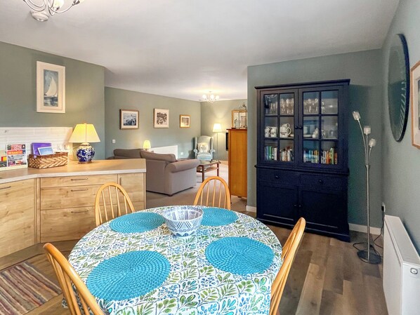 A cozy living room with a sofa, a dining table with chairs, a cabinet with glass doors, and a lamp.