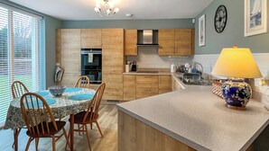 A modern kitchen with wooden cabinets, a dining area with a table and chairs, and a central island with a lamp. - Northbeach Apartment B (Prestwick)