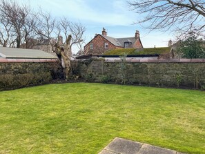 A stone wall, a grassy lawn, and a brick house with chimneys.