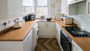 A compact kitchen with white cabinets, a wooden countertop, a microwave, a kettle, and a washing machine. - Sea Haven is a one bedroom apartment in Paignton, just steps from the seafront. (Paignton)