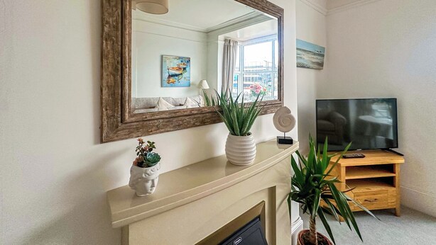 A living room with a fireplace, a television on a wooden stand, and a large mirror on the wall. - Sea Haven is a one bedroom apartment in Paignton, just steps from the seafront. (Paignton)