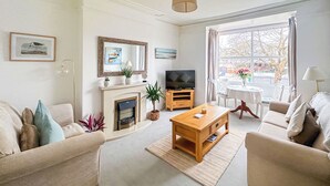 A living room with a fireplace, sofas, a coffee table, and a television. - Sea Haven is a one bedroom apartment in Paignton, just steps from the seafront. (Paignton)