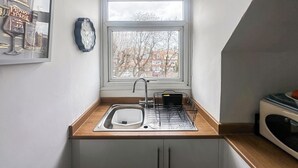 Ett litet kök med ett fönster, en diskho, en mikrovågsugn och en klocka på väggen.