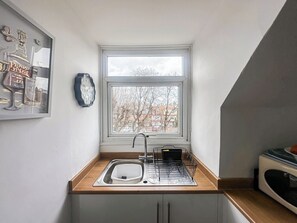 Eine kleine Küche mit Fenster, Spüle, Mikrowelle und einer Uhr an der Wand.