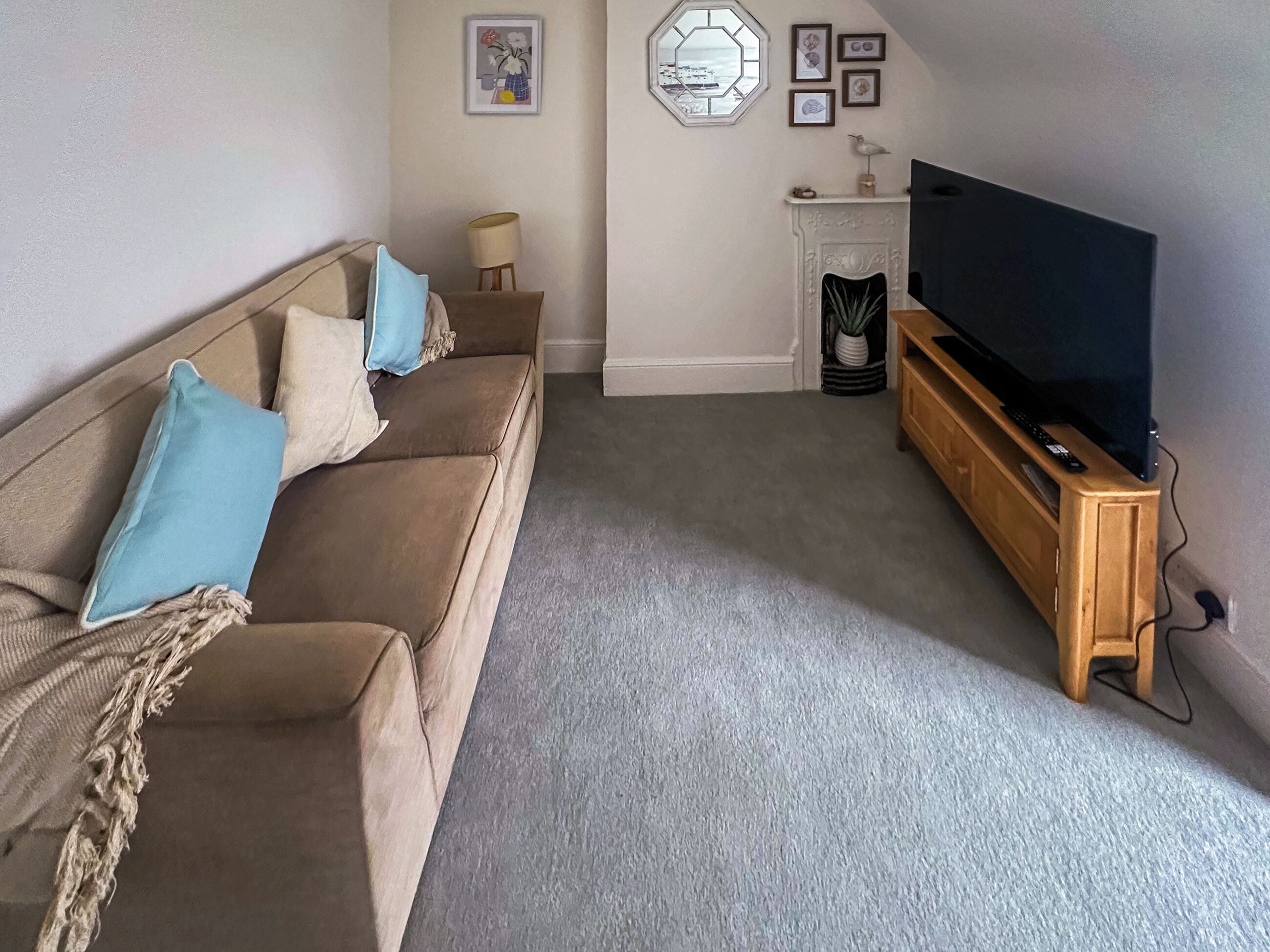 Een woonkamer met een beige bank, een televisie op een houten dressoir, een open haard en een raam met uitzicht.