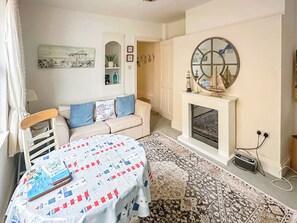 Un salón acogedor con un sofá color beige, una alfombra estampada, una mesita con un libro, una chimenea y un espejo decorativo.