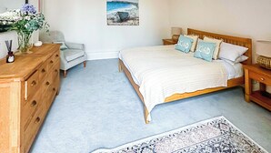 A bedroom with a bed, dresser, chair, and a painting on the wall. - Ocean Breeze - UK47847 (Paignton)