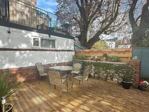 Un patio con una mesa y sillas, rodeado de plantas en macetas y un muro de ladrillo.