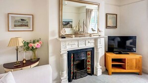 A living room with a white fireplace, a television on a wooden stand, and framed artwork on the walls. - Ocean Breeze - UK47847 (Paignton)