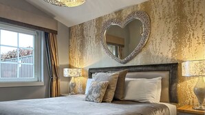Un dormitorio con una cama grande, un espejo con forma de corazón y dos lámparas de noche.