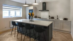A modern kitchen with a large island, bar stools, pendant lighting, and a view of the outdoors. - 2 bedroom accommodation in Chirk, near Llangollen (Chirk, near Llangollen)