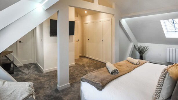 A modern bedroom with a sloped ceiling, a large bed, a TV mounted on the wall, and a walk-in closet. - 2 bedroom accommodation in Chirk, near Llangollen (Chirk, near Llangollen)