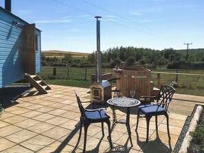 Een terras met een houten tafel en stoelen, een barbecue en een blauw gebouw op de achtergrond.