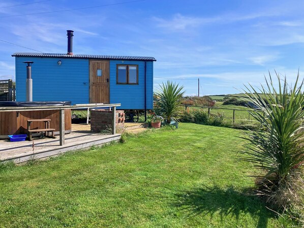 Een klein blauw huis met een houten terras, een jacuzzi en een gazon.