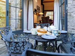 A round table with a loaf of bread, teapot, cups, and plates on a balcony with stone walls and a view into the interior. - 2 bedroom accommodation in Silverdale (Silverdale)