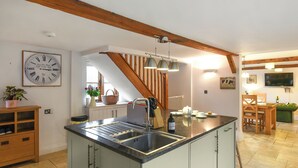 Una cucina con isola centrale, travi in legno, un orologio e zona pranzo con televisore.