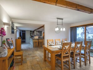 A dining area with a wooden table and chairs, a kitchen in the background, and a view through a large window. - 3 bedroom accommodation in Staunton-on-Wye (Staunton-on-Wye)