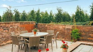 Patio esterno con tavolo rotondo e sedie in vimini, circondato da un muro in mattoni e piante in vaso.