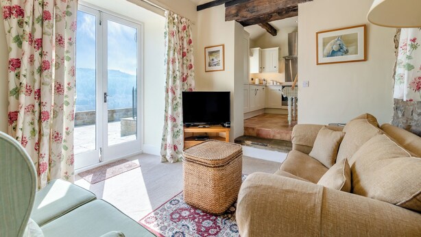 Ein Wohnzimmer mit einer Couch, einem Fernseher, einem Korbwäschesammler und Blick auf einen Balkon.