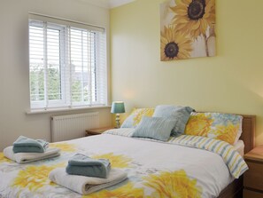 A bedroom with a bed, a window with blinds, a radiator, a bedside lamp, and a painting of sunflowers. - 6 bedroom accommodation in Llanon, near Aberaeron (Llanon, near Aberaeron)