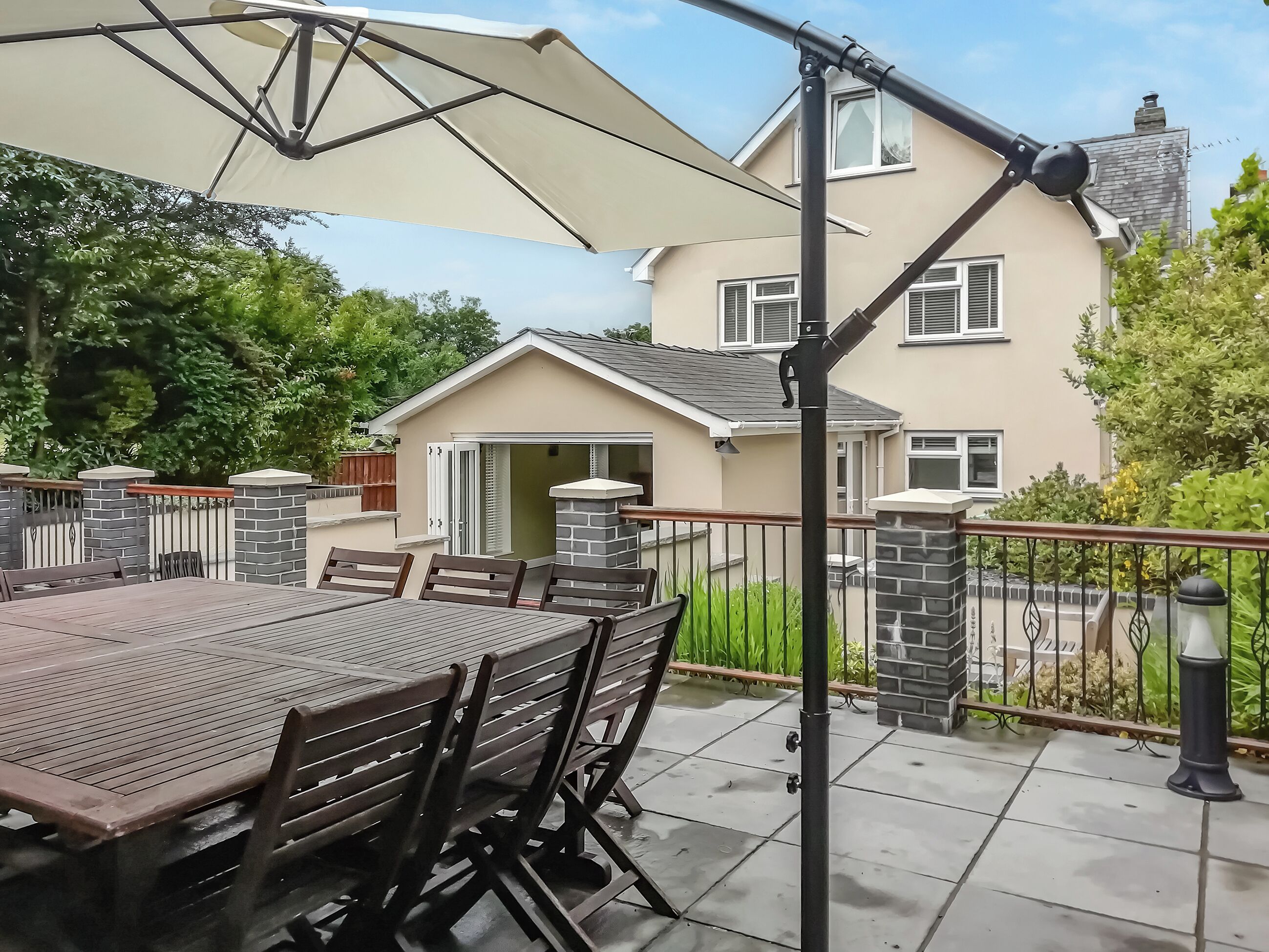 Eine Terrasse im Freien mit Tisch, Stühlen und einem großen Sonnenschirm, mit einem Haus im Hintergrund.