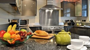 Une cuisine moderne avec des appareils en acier inoxydable, un panier de fruits, une théière et des tasses blanches posées sur le comptoir.