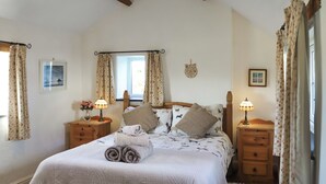 Un dormitorio ordenado con cama, dos mesitas de noche con lámparas, una ventana con cortinas y un pequeño adorno en la pared.
