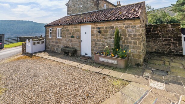 A stone cottage with a tiled roof, a white door, and a bench outside. - Manor House Farm Cottage - UK49537 (Troutsdale near Scarborough)
