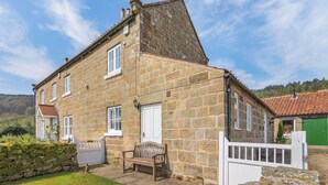 A stone house with a sloped roof, a white door, and a bench outside. - Manor House Farm Cottage - UK49537 (Troutsdale near Scarborough)