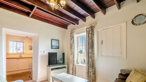A living room with a TV, a dining table, a sofa, and a kitchen area with a window. - Manor House Farm Cottage - UK49537 (Troutsdale near Scarborough)