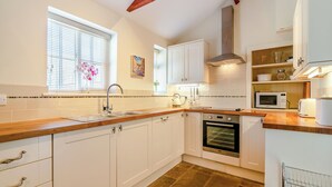 A modern kitchen with white cabinets, a wooden countertop, a built-in oven, and a window with blinds. - Manor House Farm Cottage - UK49537 (Troutsdale near Scarborough)