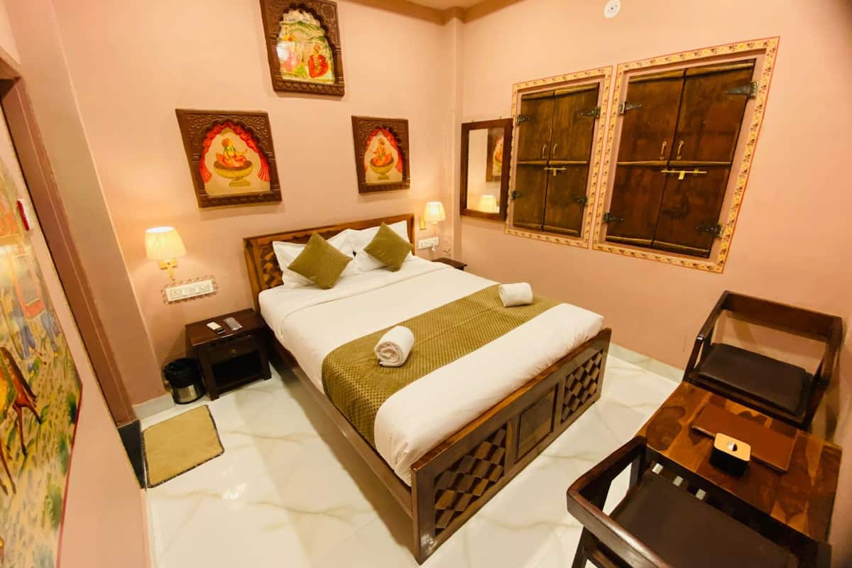 Une chambre d’hôtel avec un lit, des tables de chevet, un bureau et une chaise. Des lampes murales et des tableaux encadrés sont accrochés au mur au-dessus du lit.
