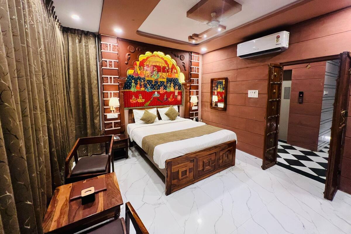 Une chambre d’hôtel comprenant un lit, un bureau, une chaise, un climatiseur fixé au mur et une porte donnant sur un sol à carreaux noirs et blancs.