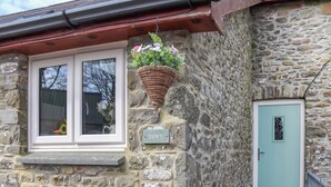 Un bâtiment en pierre avec une fenêtre, un pot de fleurs suspendu et une porte portant l’inscription « TOWY ».